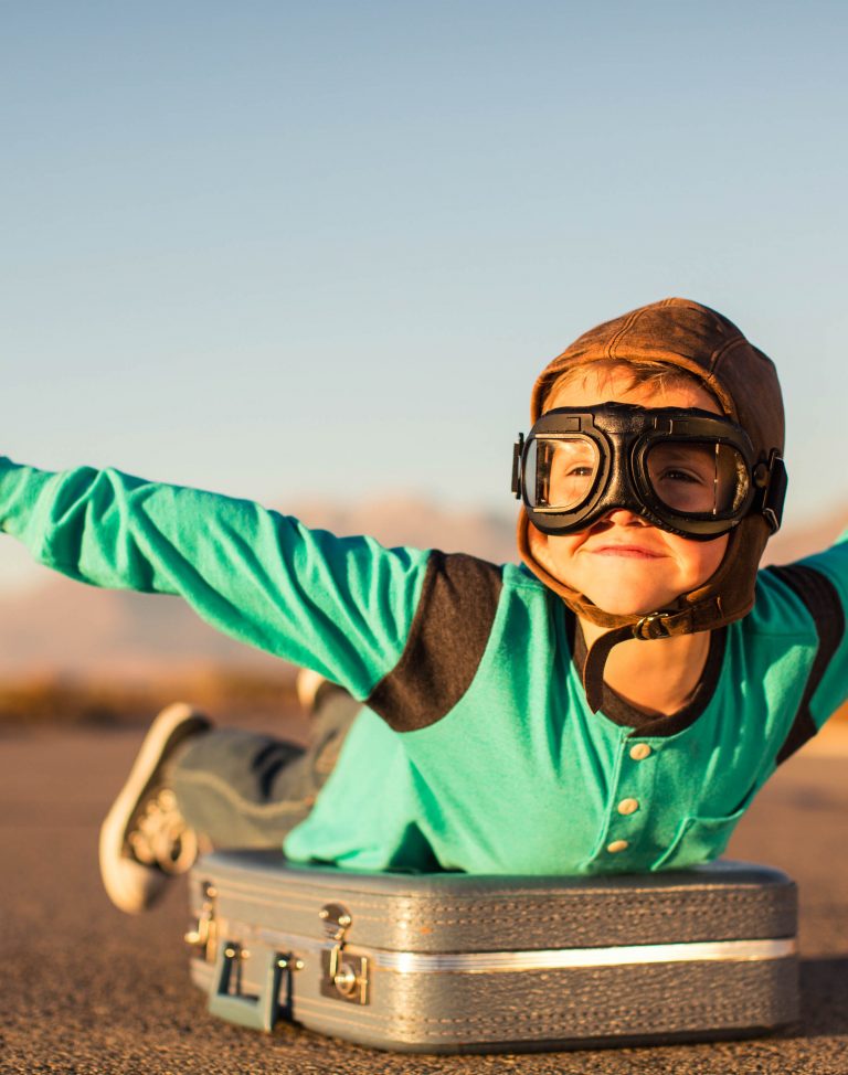 Young Boy with Goggles Imagines Flying on Suitcase